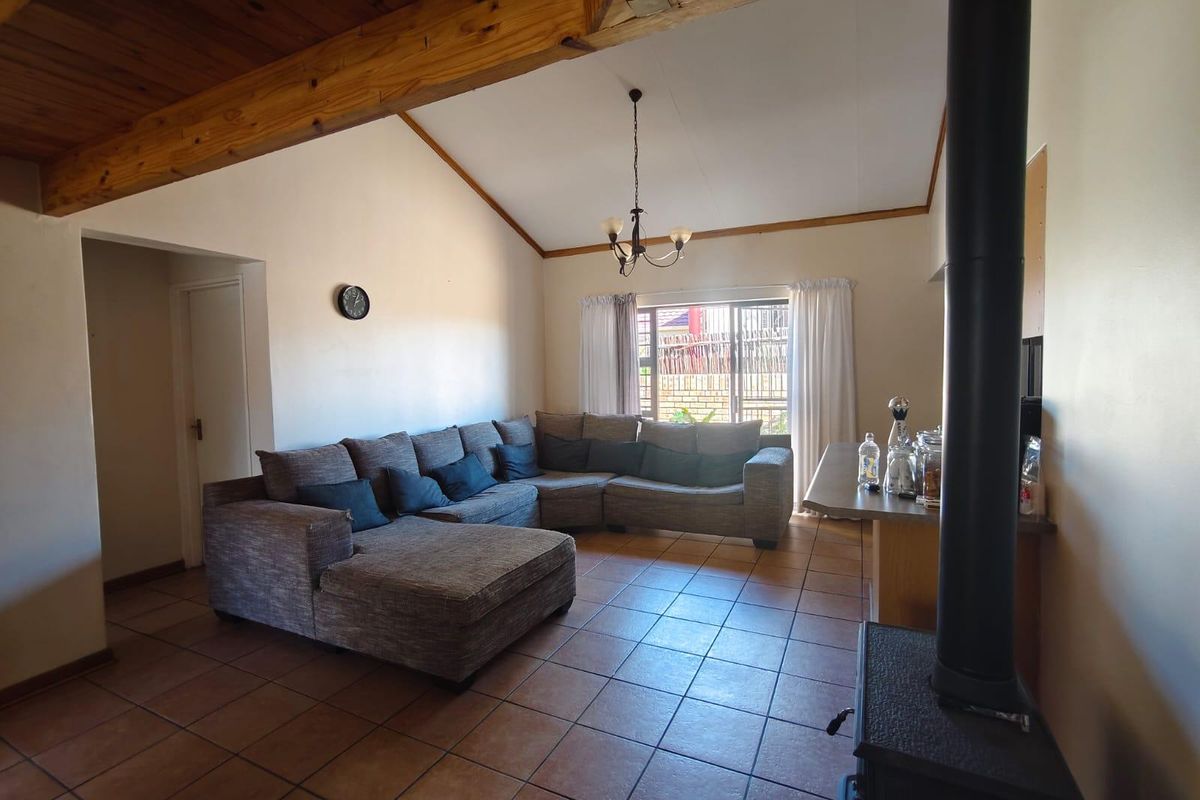 Spacious living room featuring a vaulted ceiling with exposed timber beams, tiled flooring, and a cozy freestanding fireplace.