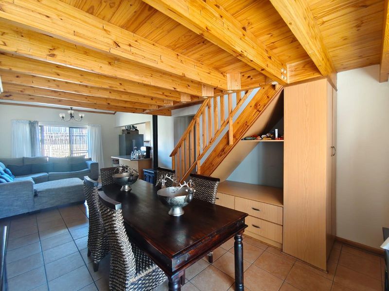 Open-plan living and dining area featuring exposed timber ceiling beams, a wooden staircase with integrated storage, and tiled flooring throughout.