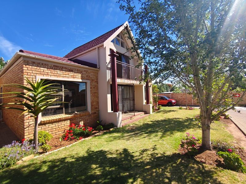 A well-maintained townhouse featuring a face brick facade, a tiled roof, and an upper-level balcony, set within a landscaped garden with a paved driveway.