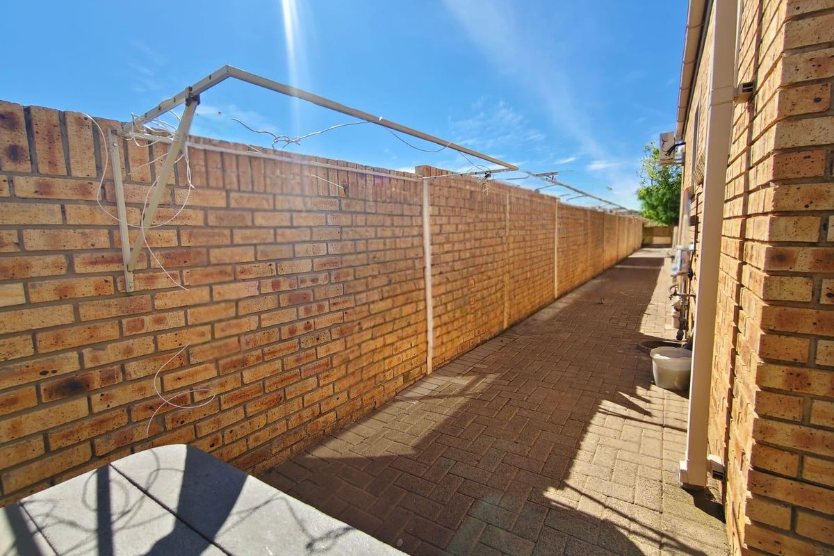 A narrow side passage featuring paved flooring and a brick boundary wall with a fixed wall-mounted clothesline.