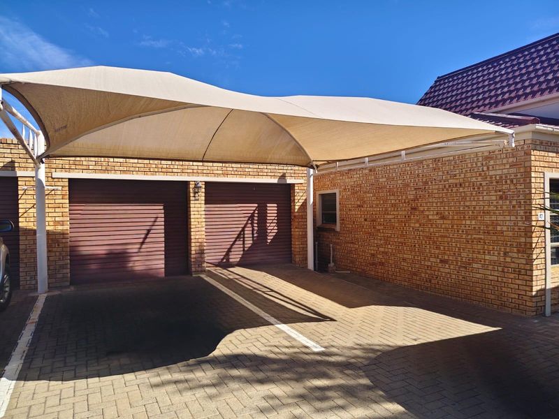 A well-maintained double garage featuring brick exterior walls, roll-up doors, and a large shade sail covering the paved driveway area.