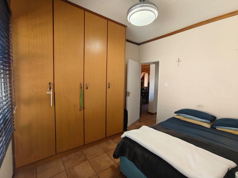 A bedroom featuring built-in wooden cupboards, tiled flooring, and a ceiling light fixture, offering a functional and well-maintained living space.