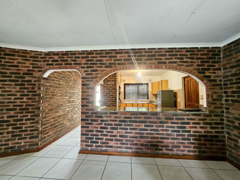 Open plan living area featuring exposed brick walls, an arched pass-through to the kitchen, granite breakfast bar, and tiled flooring throughout.