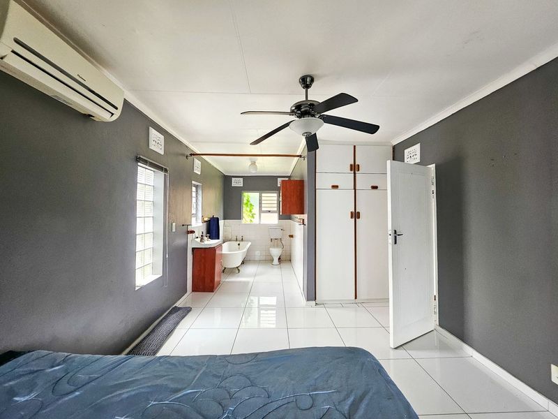 Spacious bedroom featuring an integrated en-suite bathroom with a freestanding tub, built-in cupboards, tiled flooring, and air conditioning.