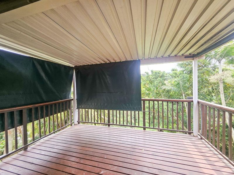 A covered outdoor balcony featuring timber decking and balustrades, offering a private space with views of the surrounding greenery.