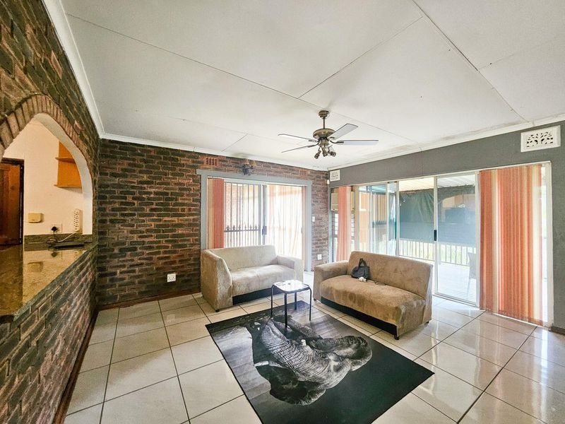 Spacious living room featuring exposed brick walls, tiled flooring, and large sliding glass doors that provide access to the outdoor patio area.