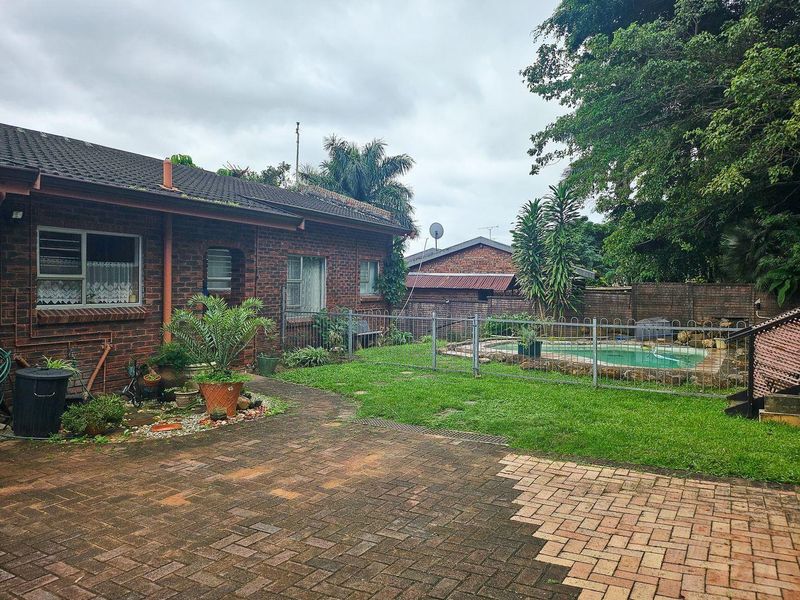 Rear exterior view of a brick house featuring a paved patio, lawn area, and a fenced swimming pool.