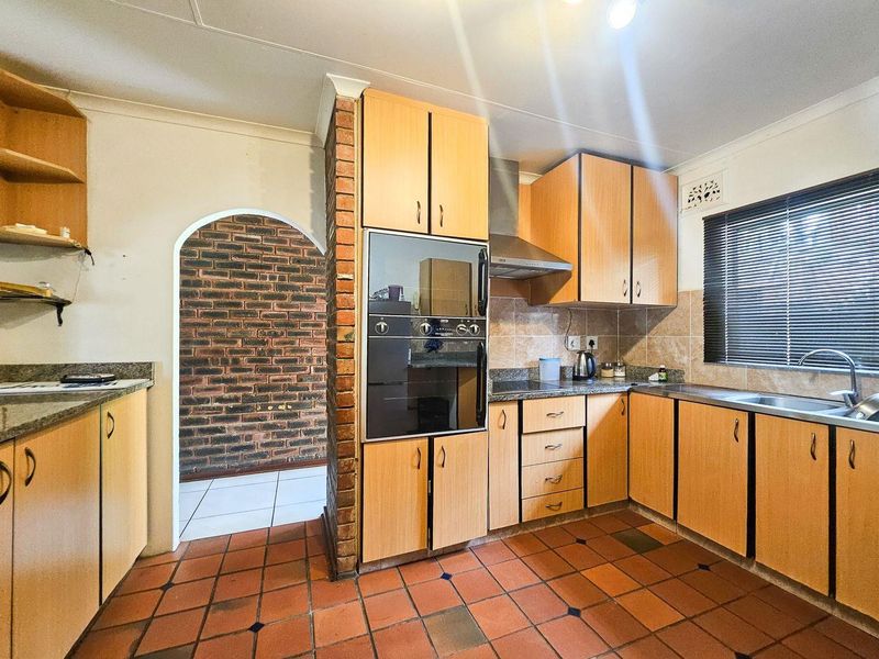 A functional kitchen featuring laminate cabinetry, granite countertops, built-in oven, extractor fan, and a distinctive exposed brick archway leading to an adjacent space.