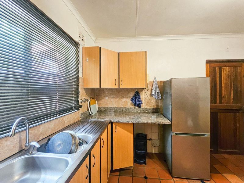 A functional kitchen featuring laminate cabinetry, granite countertops, a stainless steel double sink, and terracotta floor tiles, offering potential for modernization.