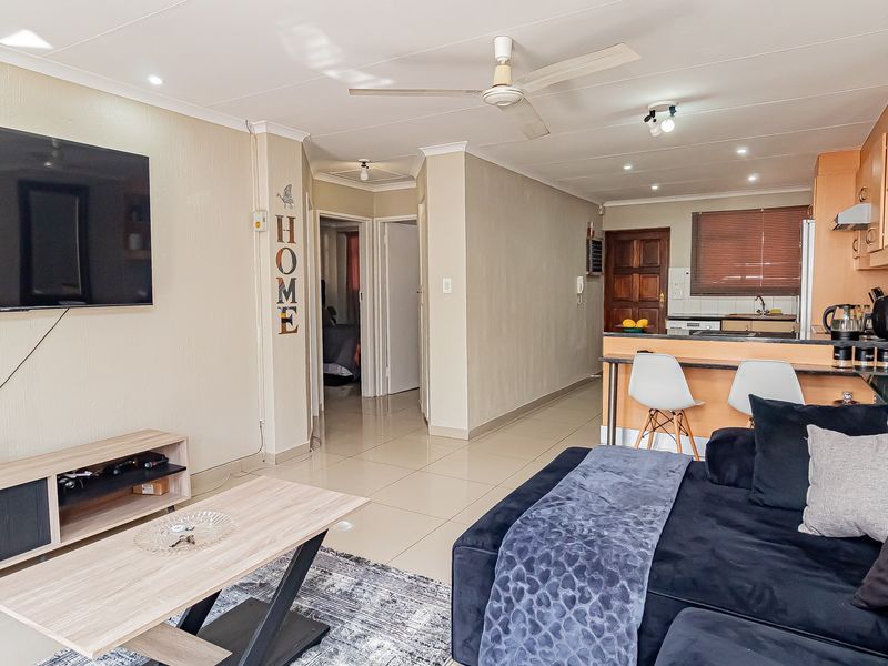 Open-plan living area featuring tiled floors, a breakfast bar, and a functional kitchen layout with integrated cabinetry and lighting.