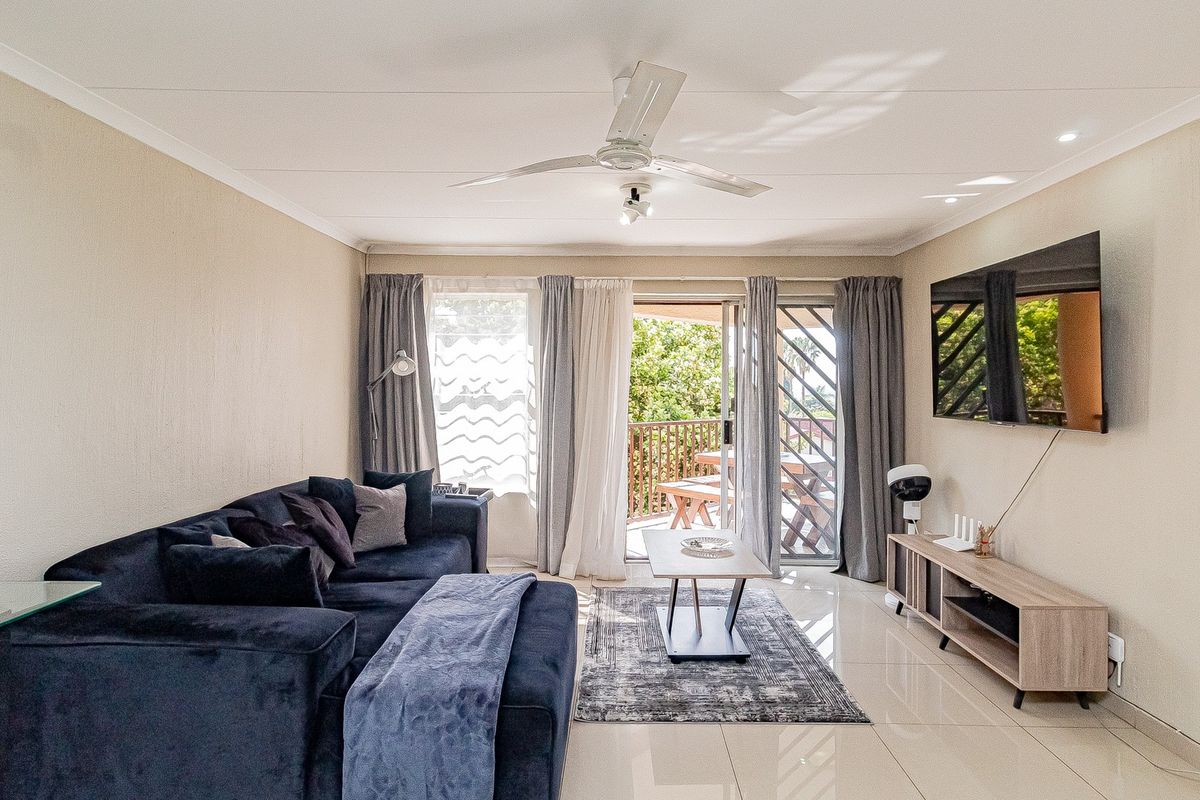 A bright and well-maintained living room featuring tiled flooring, a ceiling fan, and direct access to an outdoor balcony through sliding glass doors.