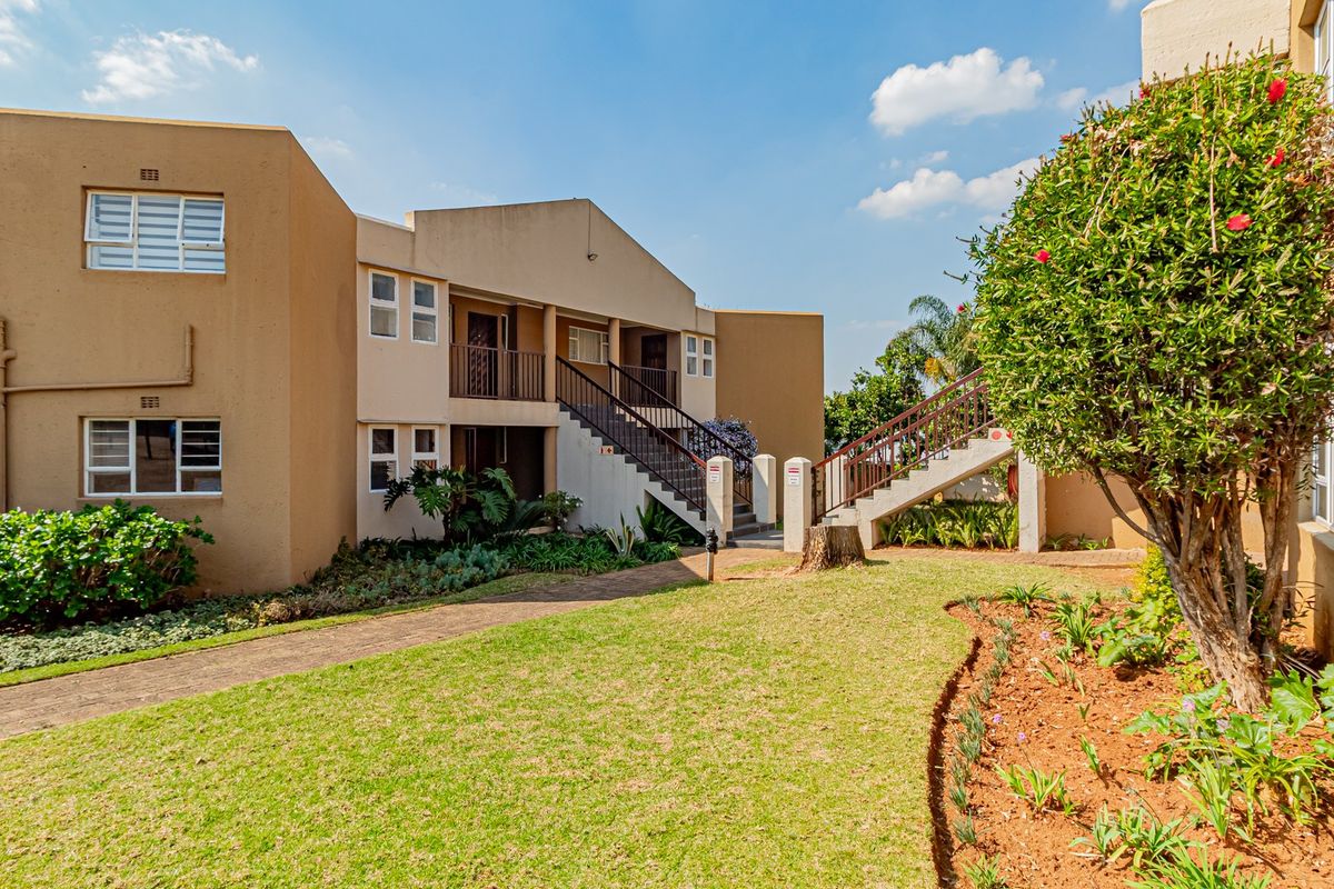 A view of the apartment complex exterior featuring a landscaped garden, paved walkways, and external staircases leading to upper-level balconies.