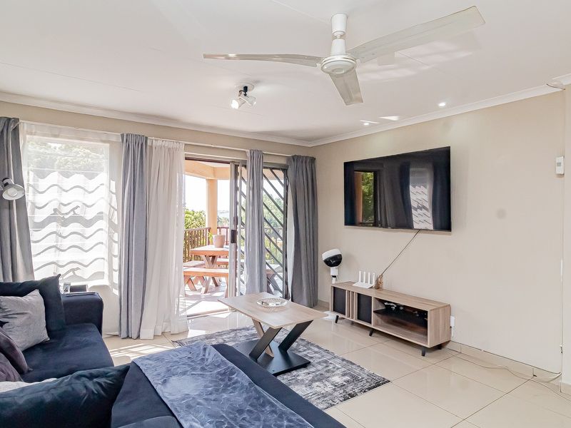 A bright living room featuring tiled flooring, a ceiling fan, and sliding glass doors that provide access to an outdoor patio area.