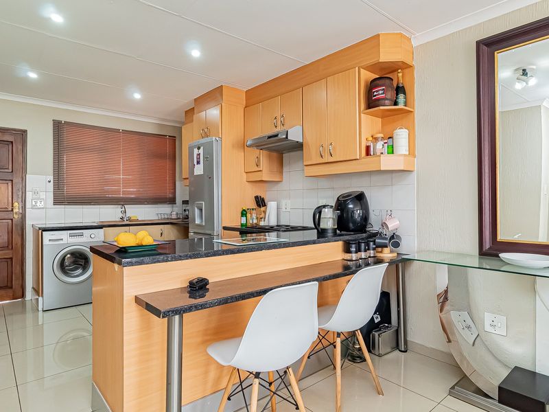 A functional kitchen featuring light wood cabinetry, granite countertops, a breakfast bar, and integrated laundry plumbing, finished with neutral tiled flooring.
