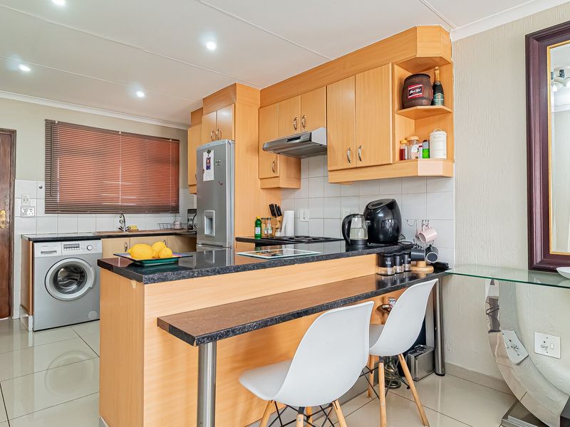 A functional kitchen featuring light wood cabinetry, granite countertops, a breakfast bar, and integrated appliances, finished with tiled flooring and recessed lighting.