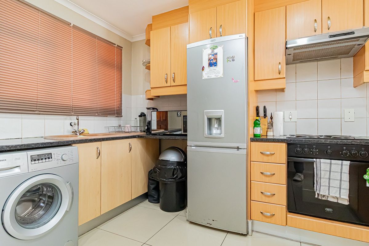 A functional kitchen featuring light wood-tone cabinetry, dark countertops, tiled backsplash, and integrated appliances including an oven and extractor fan.