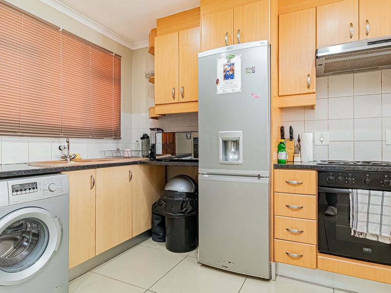 A functional kitchen featuring light wood-tone cabinetry, dark countertops, tiled backsplash, and integrated appliances including an oven and extractor fan.
