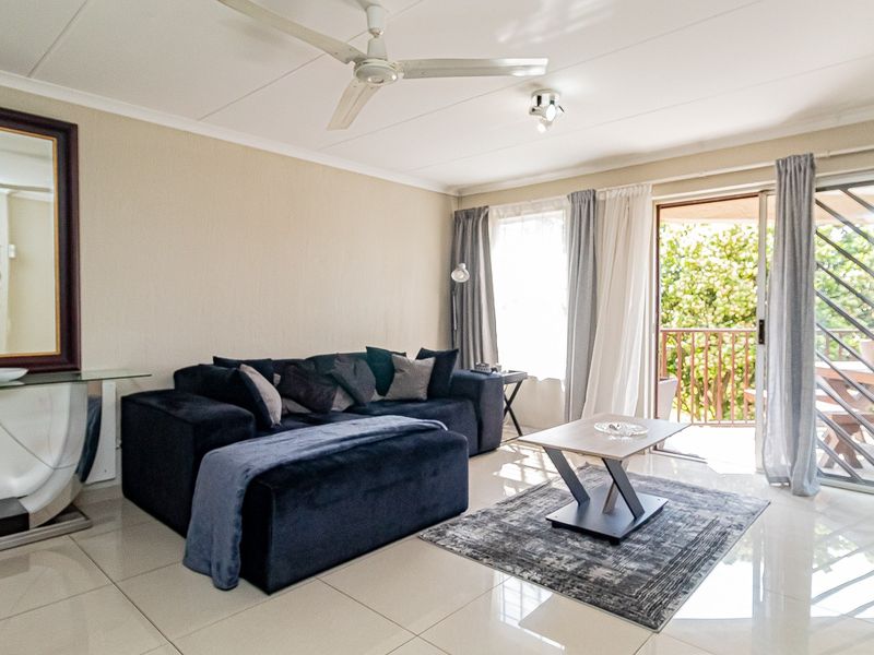 A bright living room featuring polished tiled flooring, a ceiling fan, and a sliding glass door providing access to an outdoor balcony area.