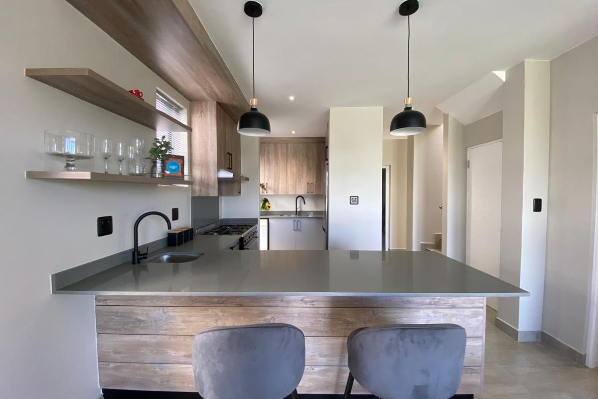 Modern kitchen featuring a central island with stone countertops, wood-finish cabinetry, floating shelves, and contemporary pendant lighting.
