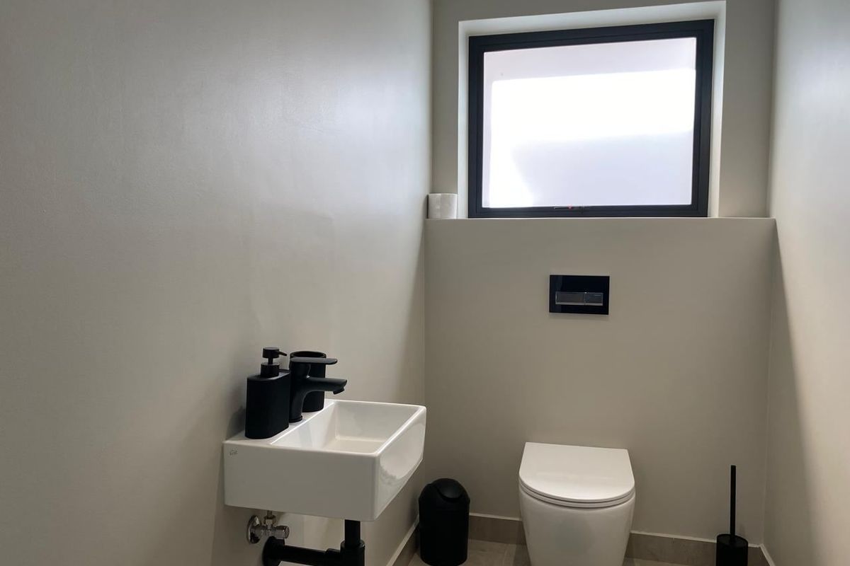 A modern, minimalist guest bathroom featuring a wall-hung toilet with a concealed cistern, a compact wall-mounted basin, and sleek black fixtures.