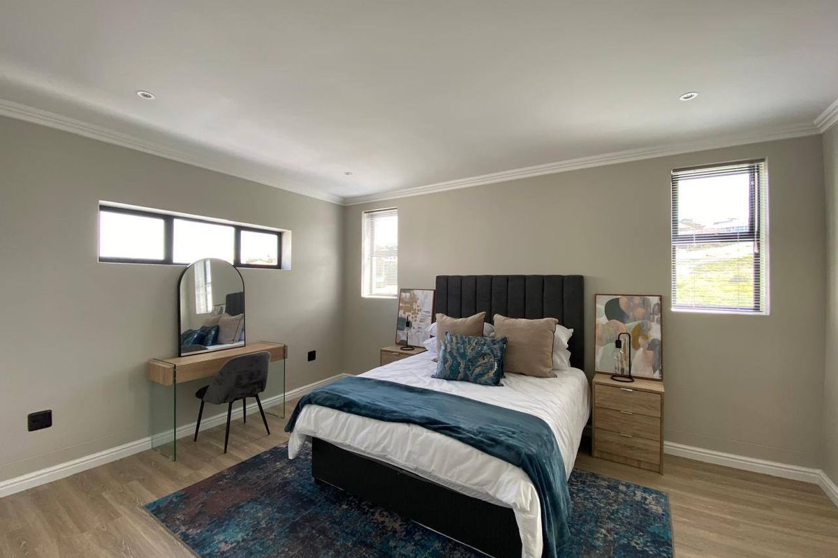 A well-maintained bedroom featuring neutral wall tones, modern laminate flooring, recessed downlighting, and multiple windows providing natural light.