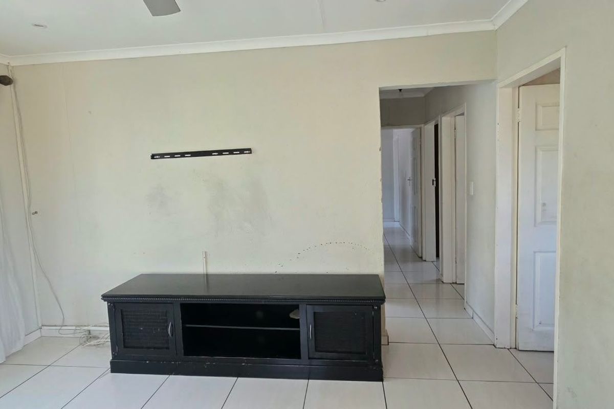 A living room featuring tiled flooring, ceiling fan, and coved cornicing, leading into a hallway with multiple internal doors.