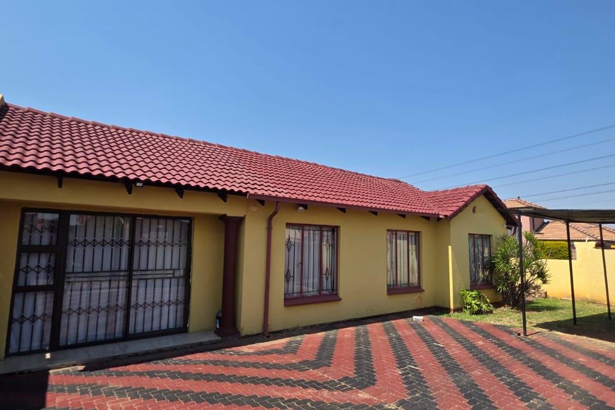 Rear exterior view of the house featuring a tiled roof, paved driveway, security gates, and a carport structure.