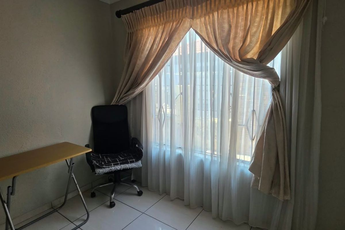 A bedroom featuring tiled flooring and a large window with security gate, providing natural light.