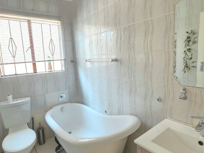 A functional bathroom featuring a freestanding bathtub, a vanity basin with chrome fixtures, and fully tiled walls, offering a clean and practical layout.