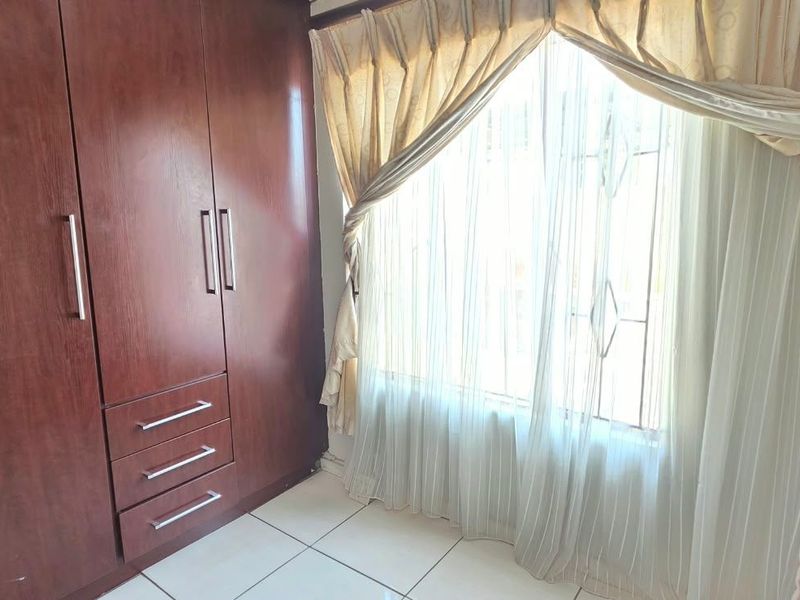 A bedroom featuring built-in wooden wardrobes, tiled flooring, and a window fitted with security bars.