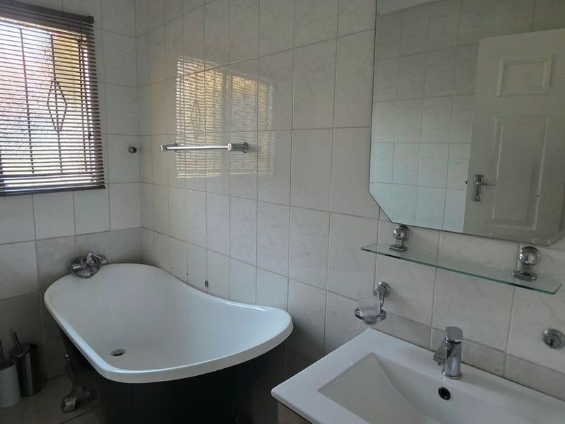 A functional bathroom featuring a freestanding bathtub, ceramic toilet, vanity basin, and wall-mounted mirror with tiled wall finishes.
