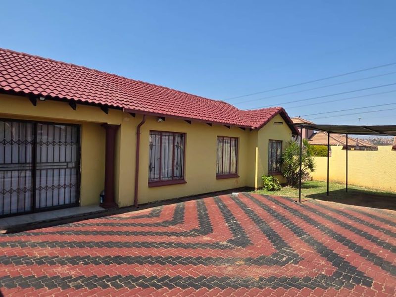 Rear view of the property featuring a paved courtyard, a covered carport area, and a single-story structure with a tiled roof and security bars.