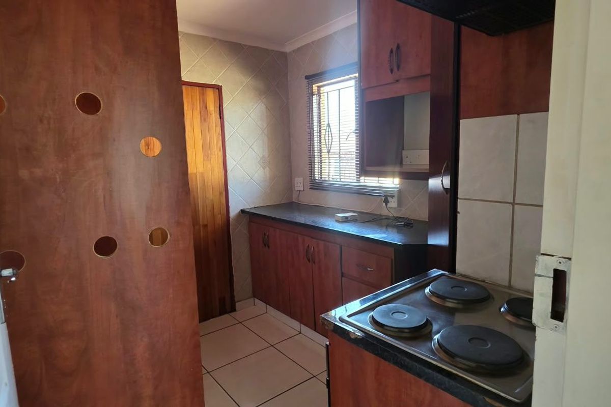 A functional kitchen featuring wooden cabinetry, tiled backsplash, and a built-in electric hob, offering a practical layout with natural light.