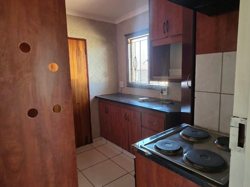 A functional kitchen featuring wooden cabinetry, tiled backsplash, and a built-in electric hob, offering a practical layout with natural light.