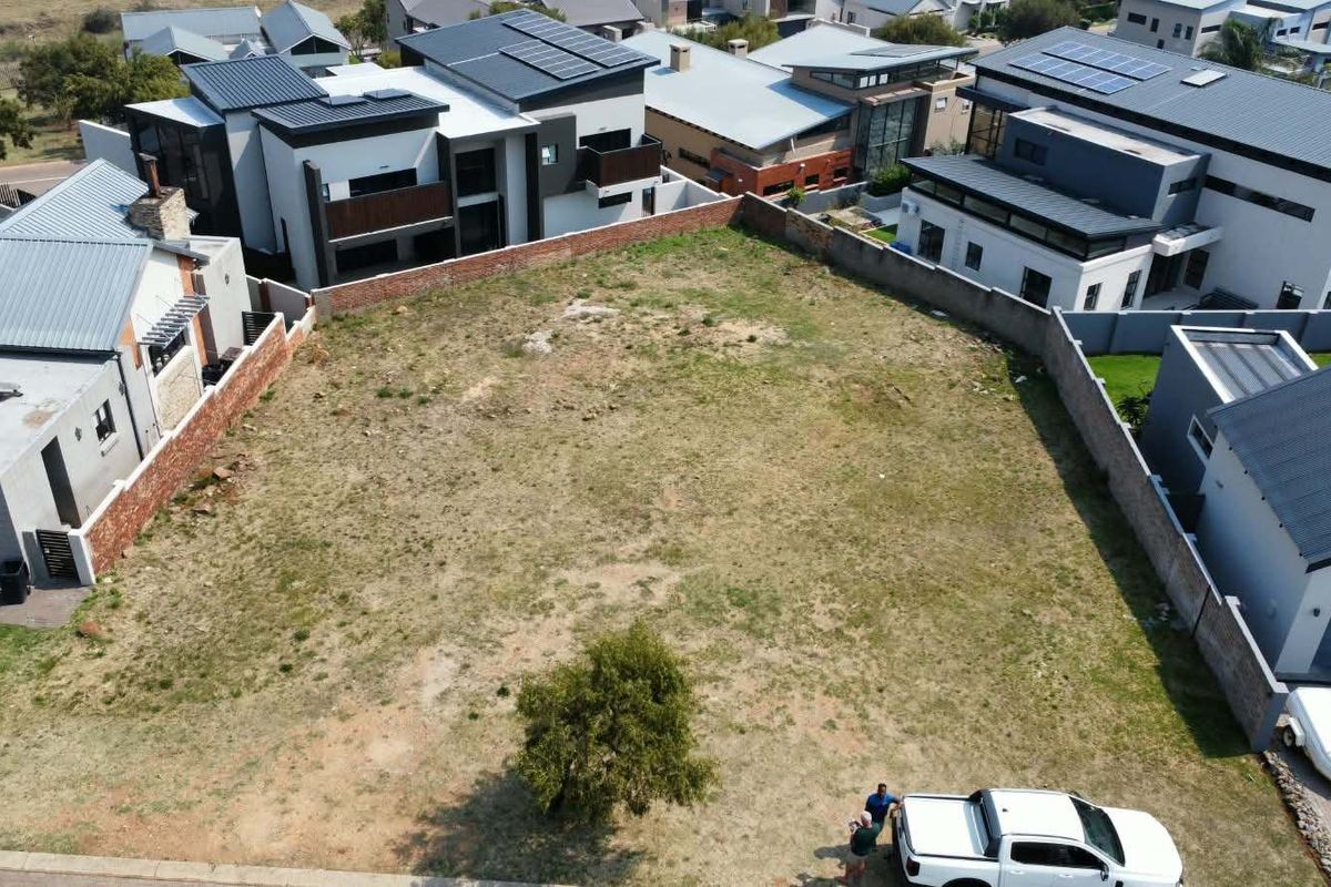 An aerial view of a vacant residential plot situated within a developed estate, surrounded by modern homes and perimeter boundary walls.