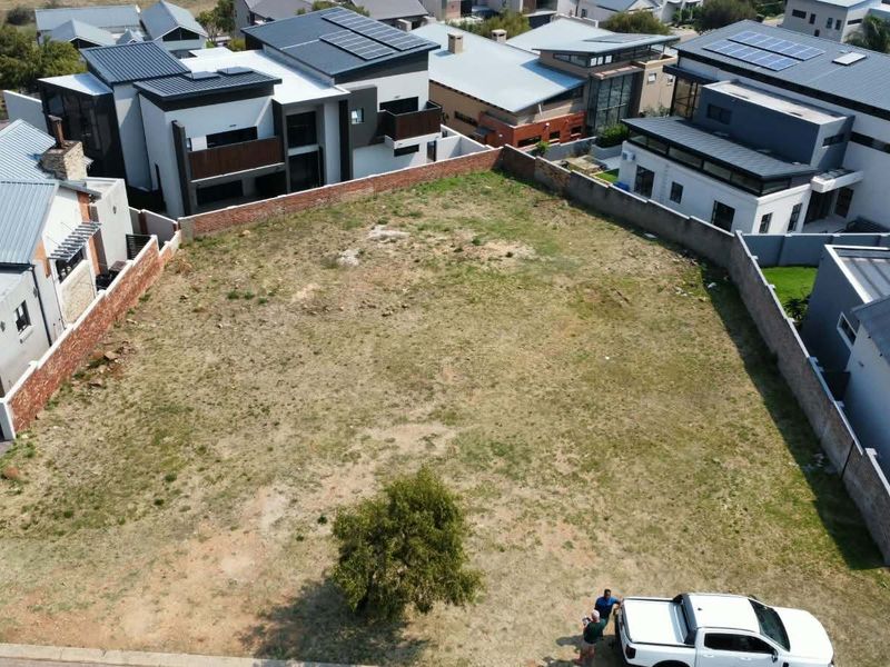 An aerial view of a vacant residential plot situated within a developed estate, surrounded by modern homes and perimeter boundary walls.