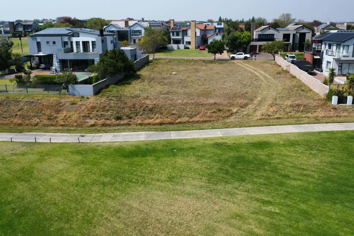 An aerial view of a vacant residential plot situated in a developed neighborhood, featuring a grass verge and paved walkway in the foreground.