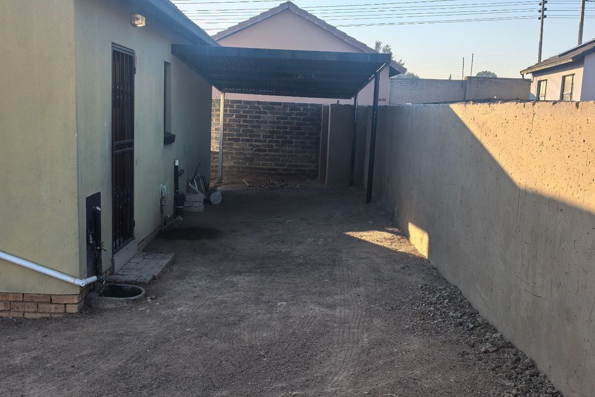 Rear exterior area featuring a carport, perimeter wall, and unpaved ground, offering potential for landscaping or paving improvements.