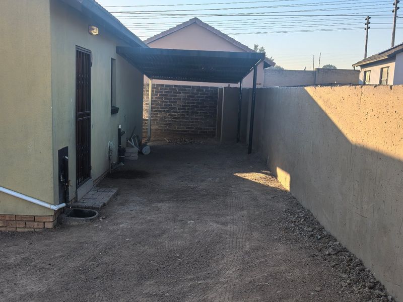 Rear exterior area featuring a carport, perimeter wall, and unpaved ground, offering potential for landscaping or paving improvements.