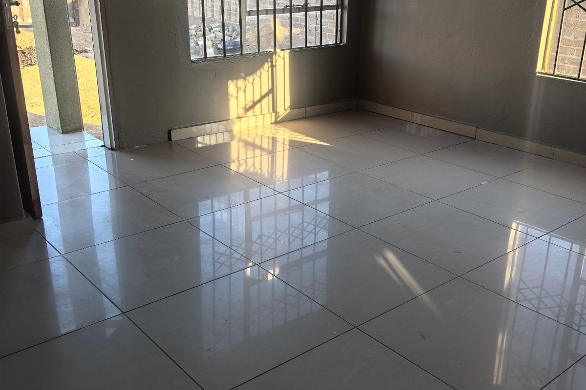 A bright, empty living area featuring polished floor tiles, security gates on windows, and direct access to the exterior.