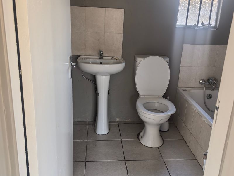 A functional bathroom featuring a pedestal basin, toilet, and bathtub with tiled finishes and security bars on the window.