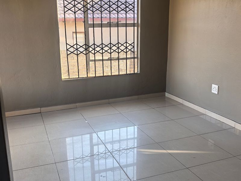 An empty bedroom featuring neutral grey walls, polished tiled flooring, and a window fitted with a security gate.
