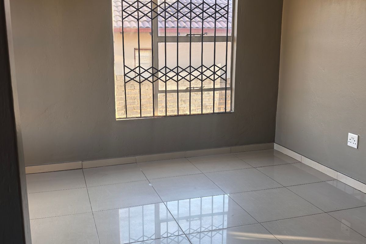 A clean, empty bedroom featuring neutral grey walls, polished tiled flooring, and a window fitted with a security gate.