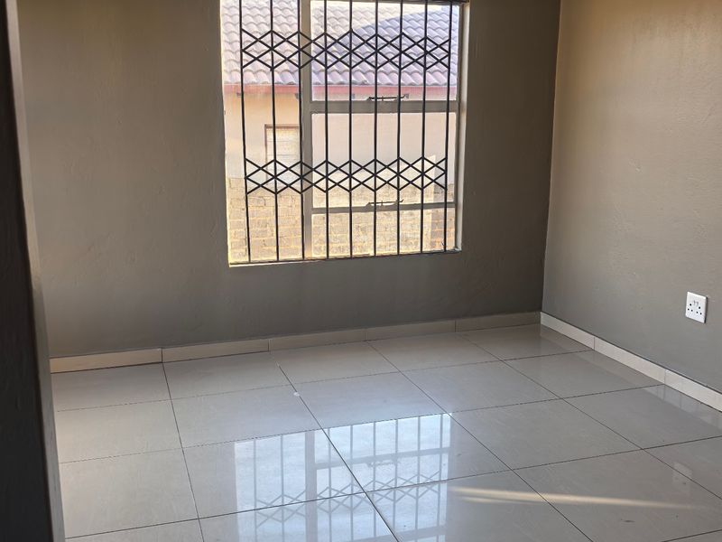 A clean, empty bedroom featuring neutral grey walls, polished tiled flooring, and a window fitted with a security gate.