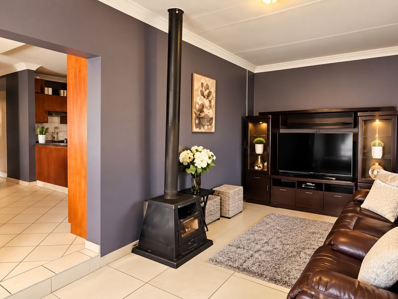 A well-maintained living room featuring a freestanding fireplace, tiled flooring, and built-in cabinetry, with an open-plan flow into the adjacent kitchen area.