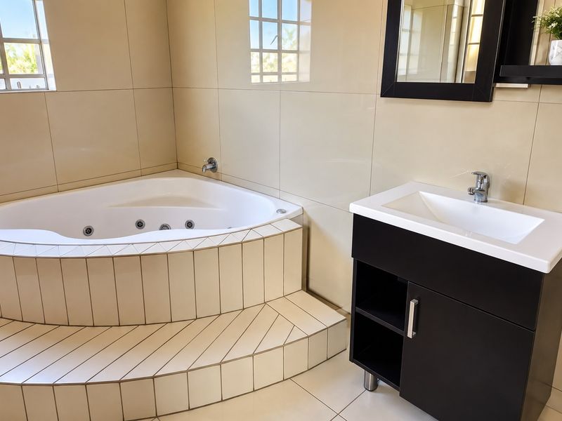 A clean, modern bathroom featuring a corner spa bath, a contemporary vanity unit with basin, and neutral wall tiling.