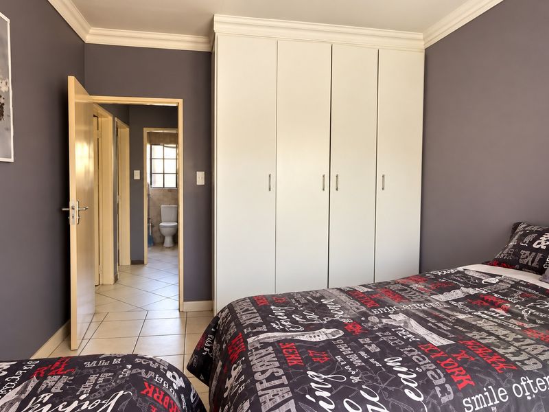 A well-maintained bedroom featuring built-in cupboards, tiled flooring, and decorative cornicing, with an adjoining hallway and bathroom visible.