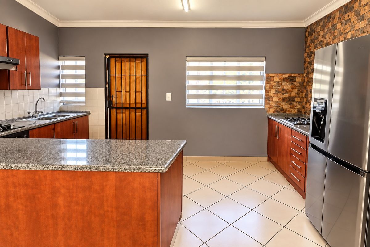 A functional kitchen featuring granite countertops, wooden cabinetry, a gas hob, and a mosaic tile backsplash, with tiled flooring and a secure rear entrance.