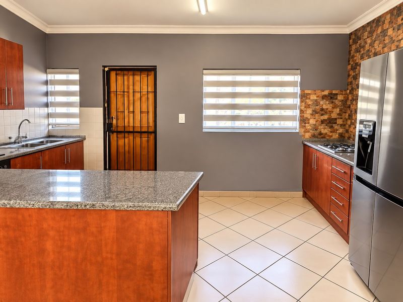 A functional kitchen featuring granite countertops, wooden cabinetry, a gas hob, and a mosaic tile backsplash, with tiled flooring and a secure rear entrance.