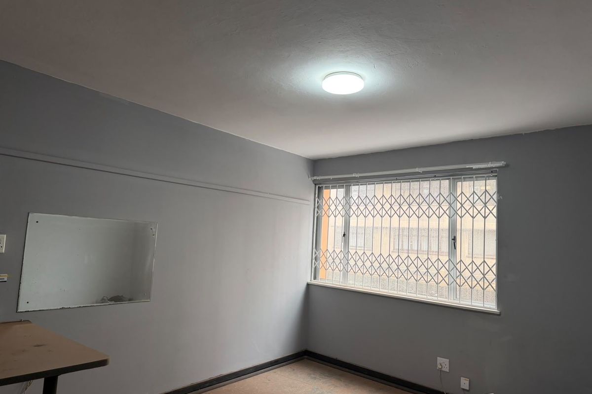 An empty bedroom featuring grey walls, a window with a security gate, and basic electrical fixtures, ready for renovation or staging.